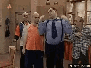 a group of men are standing in a kitchen and one of them is wearing suspenders