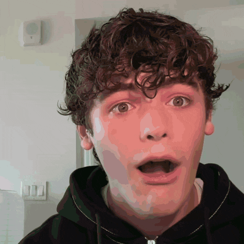 a young man with a surprised look on his face is wearing a black hoodie