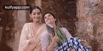 two women are sitting next to each other on a rock holding a book .