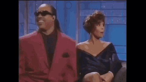 a man and a woman are sitting next to each other on a couch . the woman is wearing a purple dress .