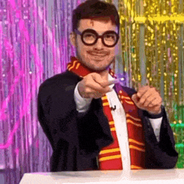 a man in a harry potter costume is pointing at the camera while wearing glasses and a scarf .