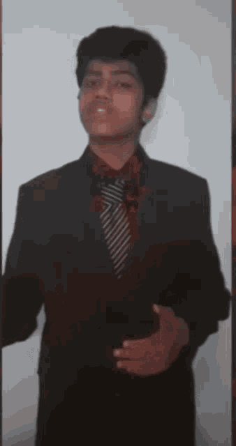 a young man wearing a suit and tie is standing in front of a white wall
