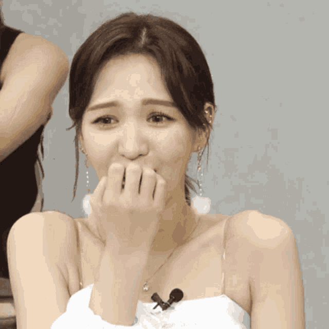 a woman covering her mouth with her hands while wearing a white top