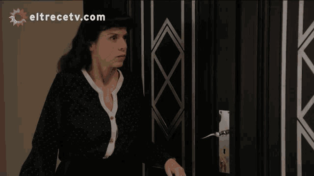 a woman stands in front of a door with eltrecetv.com written on the bottom right