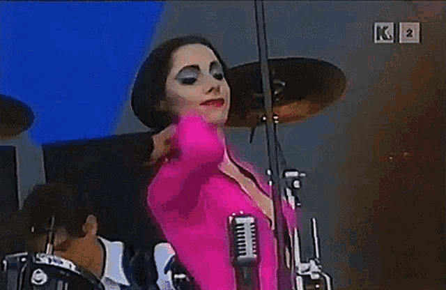 a woman in a pink jacket is singing into a microphone on stage .
