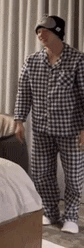a man in pajamas and a hat is standing next to a bed in a room .