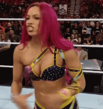 a female wrestler with pink hair is standing in a wrestling ring in front of a crowd .