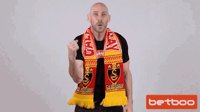 a man wearing a galatasaray scarf holds up his fist