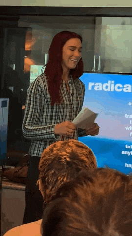 a woman with red hair stands in front of a screen that says radical