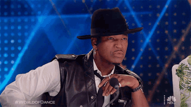a man wearing a hat is sitting in front of a microphone with the words world of dance on the bottom right