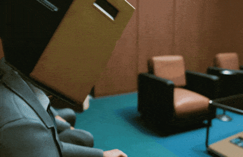 a man with a cardboard box on his head sits in a chair