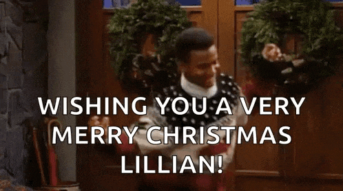 a man in a sweater is standing in front of a door with a wreath on it and laughing .