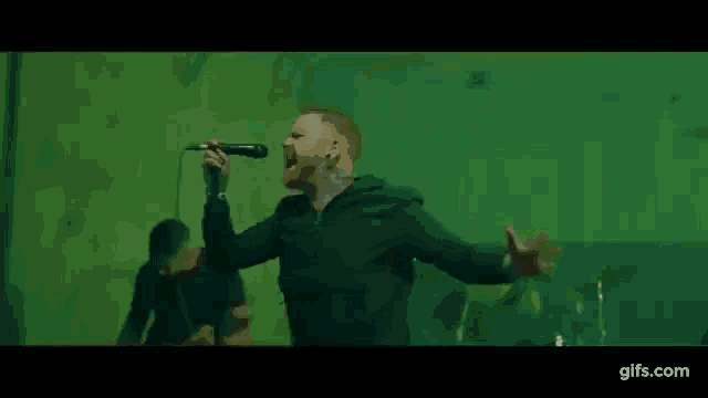 a man is singing into a microphone while standing in front of a green background .