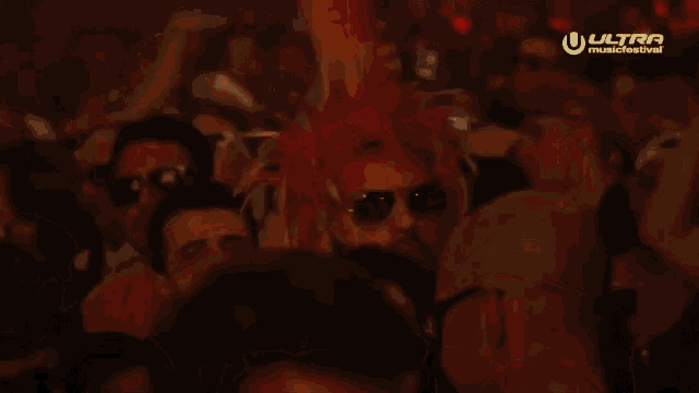 a man wearing sunglasses and a red mohawk is dancing in a crowd of people at a music festival .