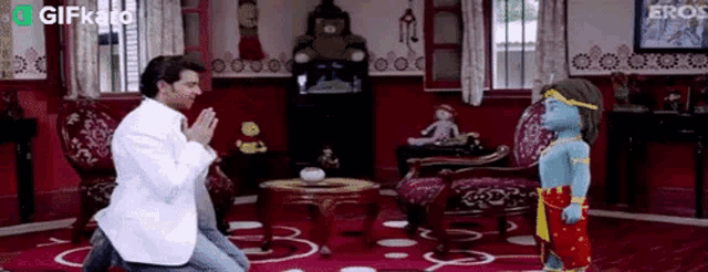 a man is kneeling down in front of a small statue of krishna in a living room .