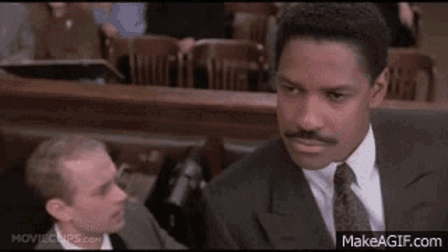 a man in a suit and tie is sitting in a courtroom with another man .