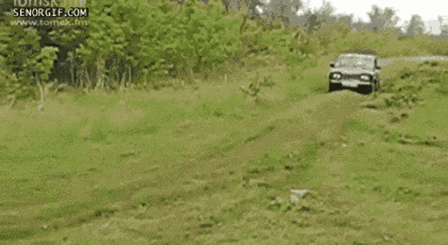 a car is driving through a grassy field and the website senogif.com is visible