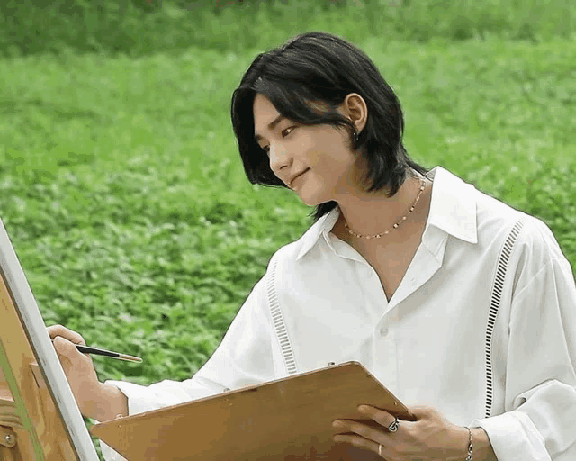 a young man with long hair is painting on an easel