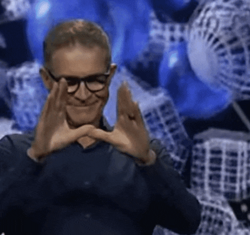 a man with glasses is making a heart with his hands .
