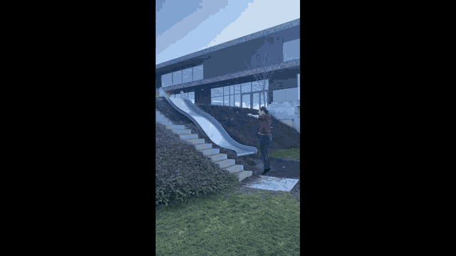 a man in a red shirt is playing on a slide in front of a building