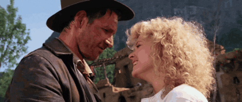 a man in a hat and a woman with curly hair are looking at each other