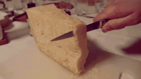 a person is cutting a large piece of cheese on a cutting board .