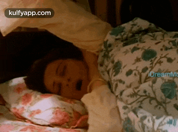 a woman is sleeping in a bed with her mouth open and a floral blanket .