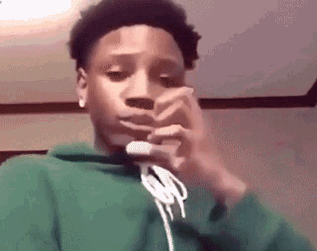 a young man in a green hoodie is smoking a cigarette in a room .