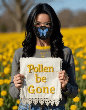 a woman wearing a face mask holds a sign that says pollen be gone