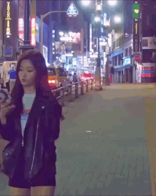a woman walking down a street looking at her phone with a sign that says ' yokohama ' in the background