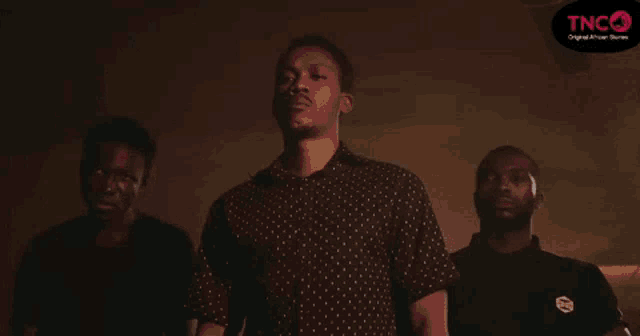 a group of three men are standing next to each other in a dark room .