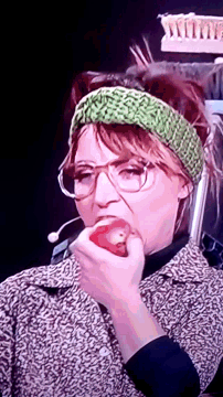 a woman wearing glasses and a green headband is holding a red object in her mouth