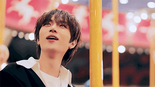 a young man is looking up at the sky while standing in front of a carousel
