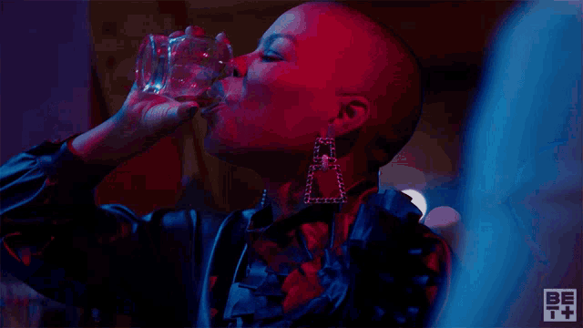 a woman with a shaved head drinking from a glass with the letter a on it