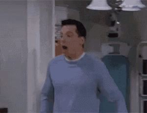 a man wearing a blue sweater is standing in a kitchen with his mouth open .