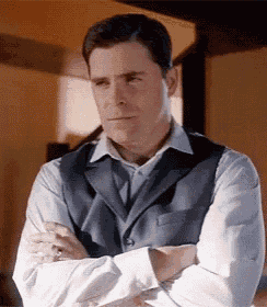 a man in a suit and vest is standing with his arms crossed and looking at the camera .