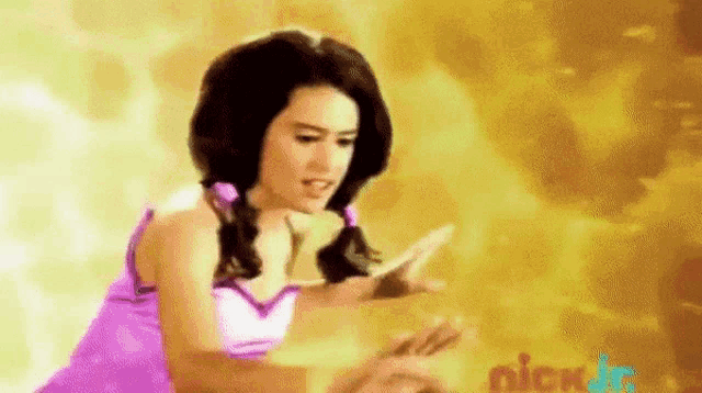 a woman in a purple dress is standing in front of a yellow background holding a cell phone .
