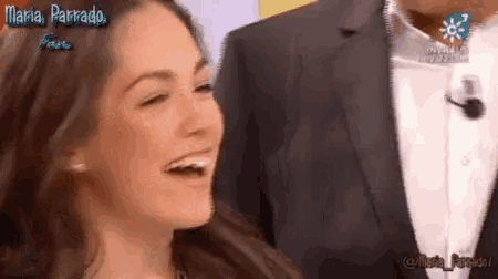 a woman is laughing while standing next to a man in a suit on a television show .