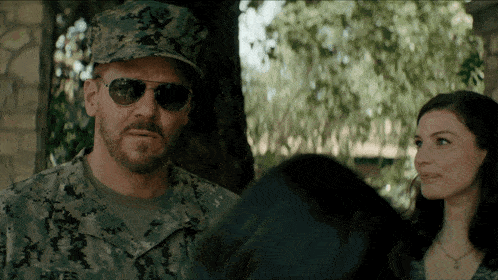 a man in a military uniform and sunglasses is talking to a woman