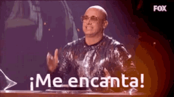a man in a sequined shirt is sitting at a table with the words me encanta written on it .