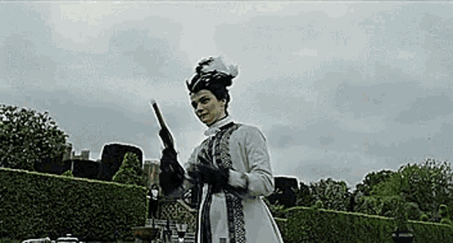 a woman in a white dress and black gloves is holding a cane in a park .