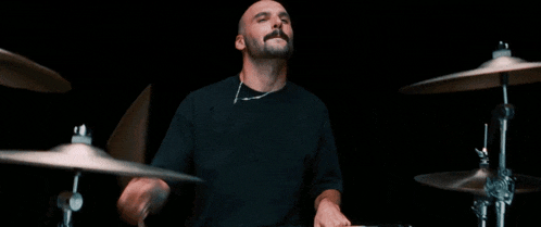 a bald man with a beard is playing a drum set in a dark room .
