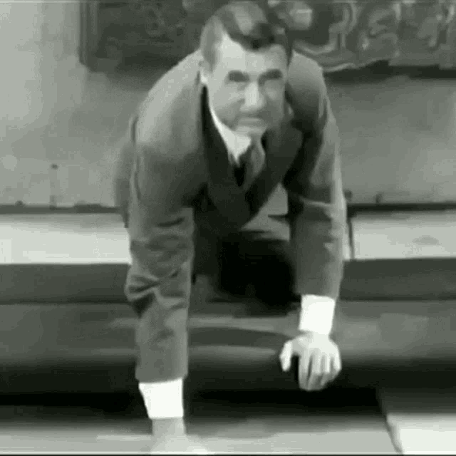 a black and white photo of a man in a suit and tie bending over .