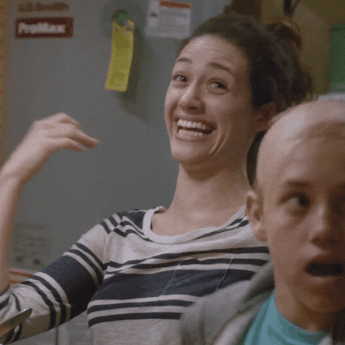 a woman laughs while sitting next to a boy with a yellow sticky note on the refrigerator door that says yelmax