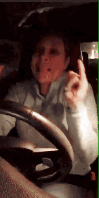 a woman is driving a car and giving a middle finger