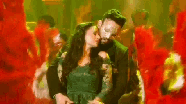 a man and a woman are dancing together in a dark room surrounded by red flowers .