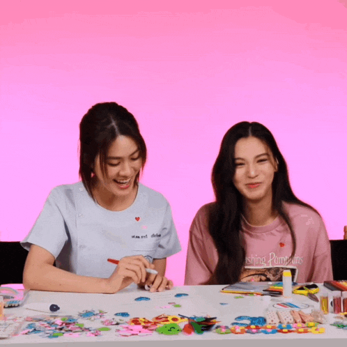 two girls are sitting at a table with a pink background and one girl is wearing a shirt that says ' shining paradise '