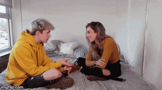 a man in a yellow hoodie sits next to a woman on a bed .