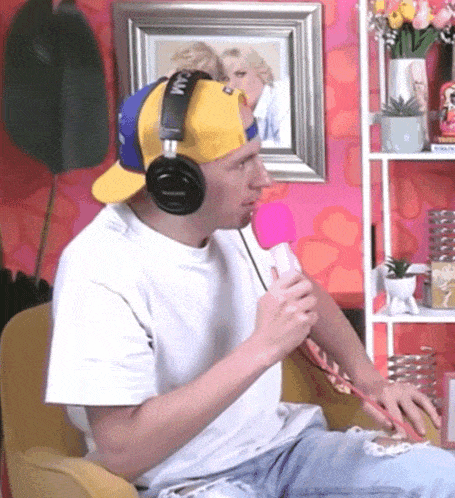 a man wearing headphones and a yellow hat holds a pink microphone