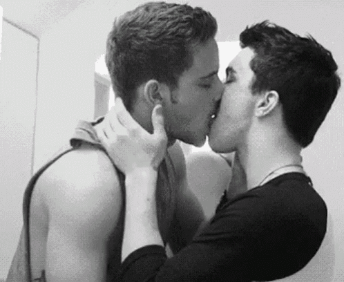 two young men are kissing in a black and white photo .